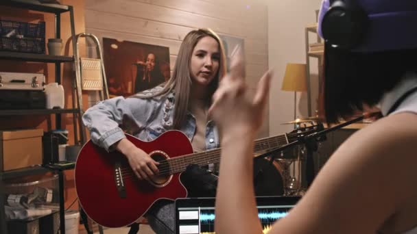 Über-die-Schulter-Medium-Slowmo von Mädchen, die akustische Gitarre im Mikrofon spielen, während sie Musik im Musikstudio im Retro-Stil aufnehmen - Filmmaterial, Video