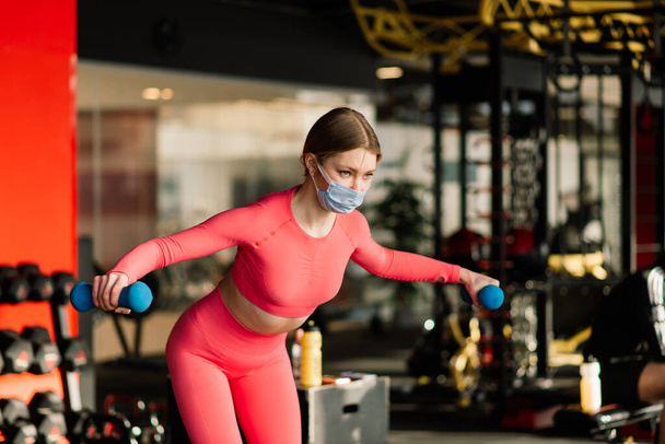 Vrouw dragen gezichtsmasker oefening in de sportschool tijdens corona virus pandermic, covid - Foto, afbeelding