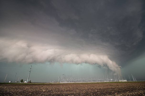 Μια σοβαρή καταιγίδα και χαμηλό ράφι σύννεφο αργαλειού πάνω από τον ηλεκτρικό εξοπλισμό και τους πόλους ισχύος. - Φωτογραφία, εικόνα