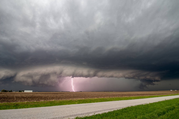 Un fulmine colpisce mentre un temporale di supercelle si avvicina ad una strada rurale. Una nuvola di scaffali segna il bordo della tempesta. - Foto, immagini