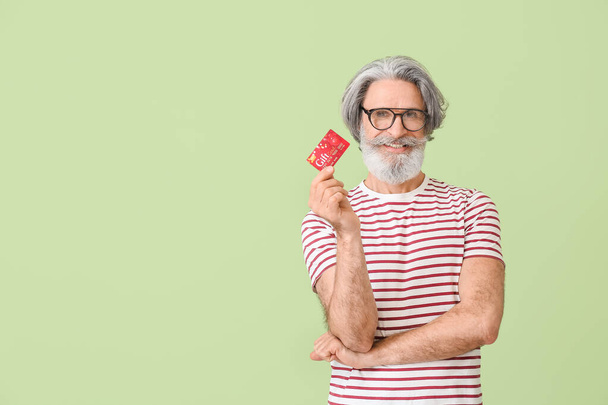 Старший мужчина с подарочной картой на цветном фоне - Фото, изображение