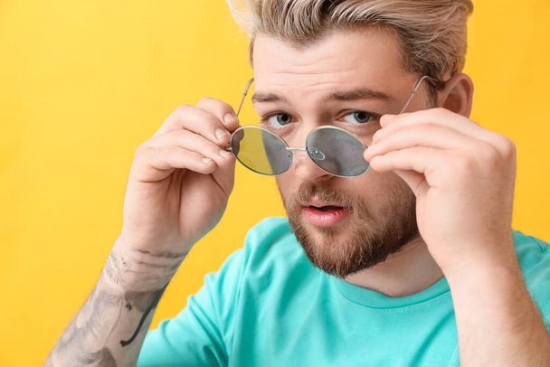 Jeune homme avec des lunettes de soleil élégantes sur fond de couleur - Photo, image