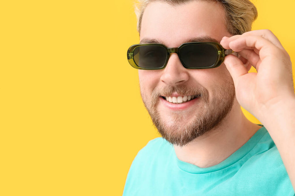 Hombre joven con gafas de sol con estilo en el fondo de color - Foto, imagen