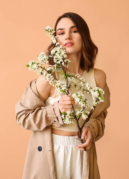Beautiful young woman with blooming spring branches on color background - Foto, Imagen