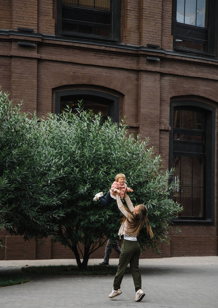 young beautiful mother with long hair with children on walk in street happiness joy fun motherhood - Photo, Image