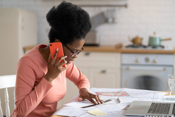 Keskittynyt musta nainen arkkitehti työstää pohjapiirros puhelun kotoa. Suunnittelija freelance - Valokuva, kuva
