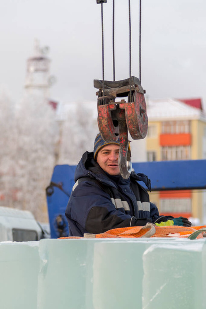Портрет рабочего в синей куртке с капюшоном на крючке грузового крана - Фото, изображение