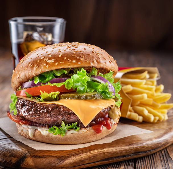 Delicious hamburger with cola and potato fries on a wooden table with a dark brown background behind. Fast food concept. - Foto, immagini
