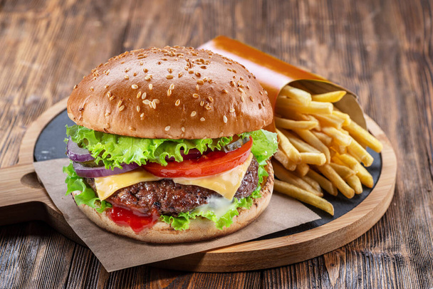 Delicious burger with potato fries on a wooden table with a dark brown background behind. Fast food concept. - Foto, immagini