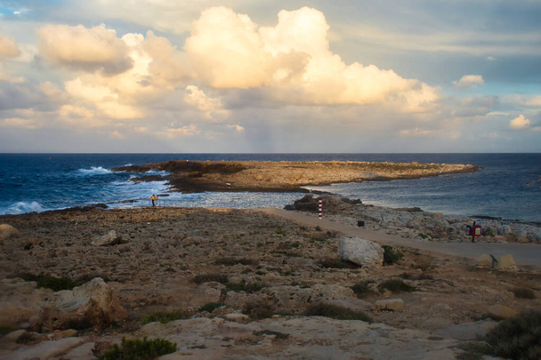 Light shining on small island in the ocean at a beach in Qawra, Malta at sunset. - Foto, imagen