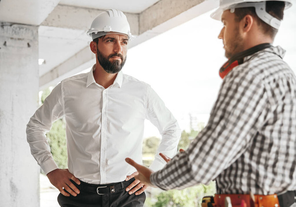 Male contractors in hardhats talking about project at construction site - Photo, Image