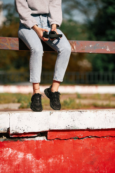 都会の外の柵の上に座ってヘッドフォンを持っている若い女性の作物の写真. - 写真・画像
