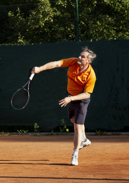 An adult man plays tennis on a street court on a sunny day. Sports and active lifestyle. Vertical. - Zdjęcie, obraz