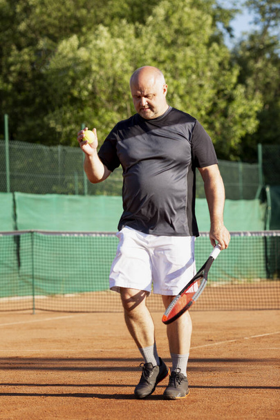 An adult man plays tennis on a street court on a sunny day. Sports and active lifestyle. Vertical. - Valokuva, kuva