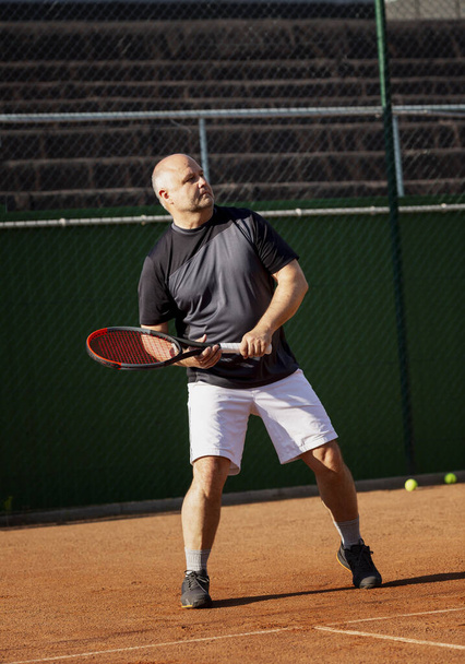 An adult man plays tennis on a street court on a sunny day. Sports and active lifestyle. Vertical. - 写真・画像