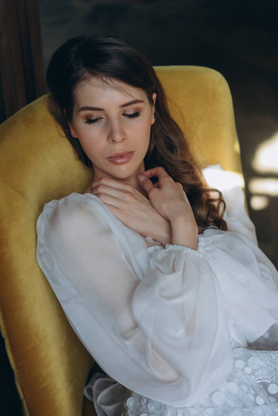  girl in a beautiful white bohemian tulle dress sitting in a chair near the balcony, closeup view of woman in a pensive mood and she looking down - Fotografie, Obrázek