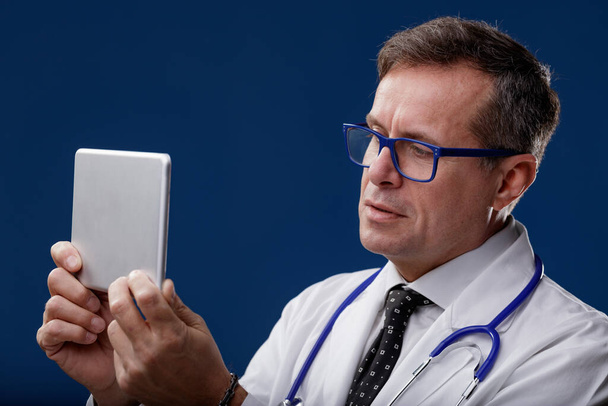 Doctor usando un estetoscopio mirando una tableta digital portátil con expresión reflexiva en un concepto de tecnología médica y salud - Foto, imagen