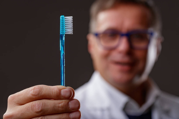 Közelkép egy barátságos fogorvos kezéről, aki egy kék fogkefét mutat be a szájhigiénia és a rendszeres fogászati ellenőrzés figyelemfelkeltő kampányaként - Fotó, kép