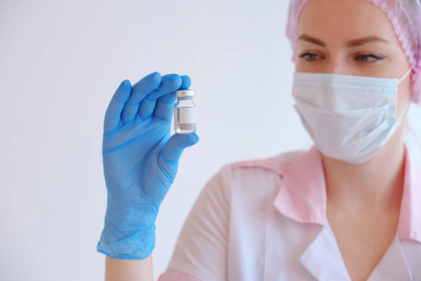 ピンクの制服を着た女医と注射器とCOVID-19ワクチンを持った青い手袋。ヘルスケアと医療の概念. - 写真・画像