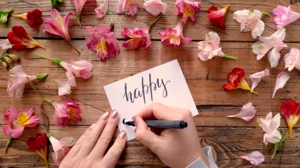 Escribir ANIVERSARIO FELIZ en una tarjeta cerca de flores vista superior  - Imágenes, Vídeo