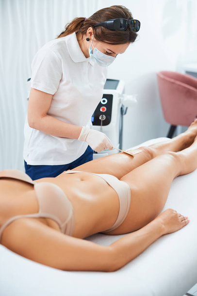Focused cosmetician removing the excess gel from the woman leg - Photo, Image