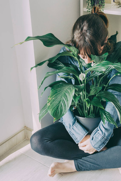 portrait of a woman with brown hair sits on the floor of her house and hugs a plant from a pot - Фото, зображення