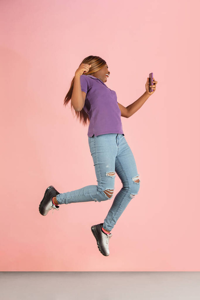 One happy African young girl jumping isolated on pink studio background. - Фото, изображение