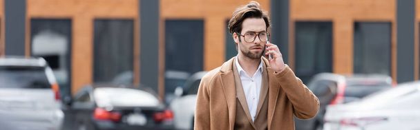 uomo d'affari fiducioso in occhiali che parla sul telefono cellulare nel parcheggio all'aperto, banner - Foto, immagini