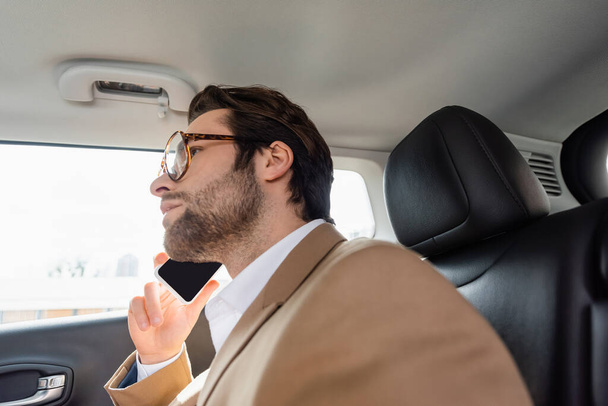 homem preocupado em óculos e terno falando no smartphone no carro - Foto, Imagem