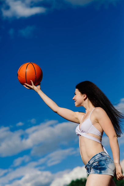 Молода атлетична жінка, у верхній і синій штани, грає з м'ячем на баскетбольному майданчику на відкритому повітрі
. - Фото, зображення