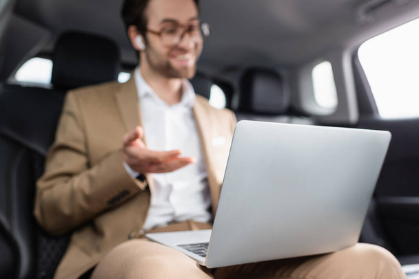 blurred businessman in glasses and wireless earphones having video call in car  - Foto, afbeelding
