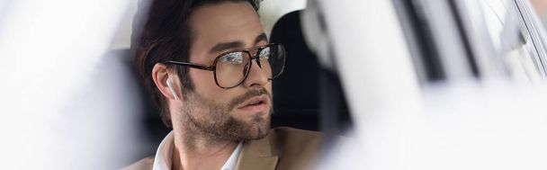 üzletember szemüvegben és vezeték nélküli fülhallgató autóban, banner - Fotó, kép