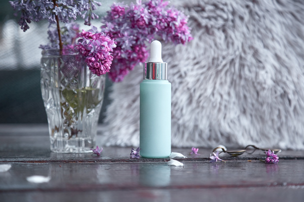 Mock up of turquoise anti age serum droplet with lilac flowers. Natural wellness cosmetic product. Dropper glass bottle mock-Up. Body treatment and spa. Natural beauty products. Personal care concept - Foto, Imagen