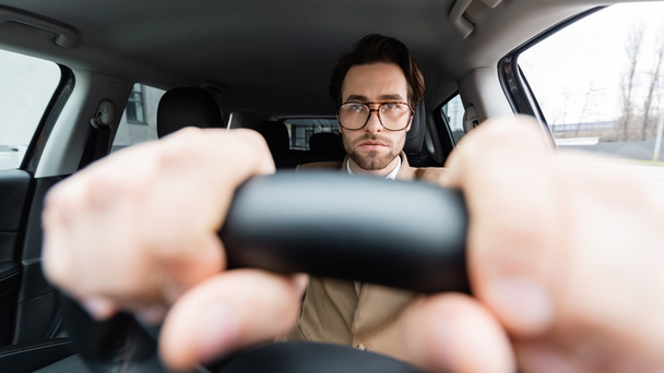 bearded man in glasses with hands on steering wheel with blurred foreground  - Foto, afbeelding