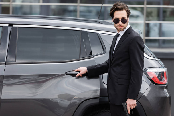 safeguard in suit and sunglasses and suit holding gun near modern auto - Photo, Image