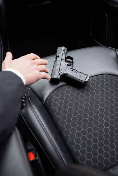 cropped view of bodyguard reaching gun on seat of modern automobile  - Foto, afbeelding