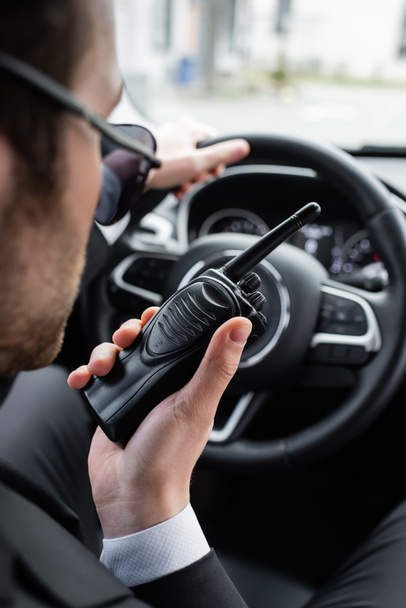 blurred bodyguard in sunglasses using walkie talkie in car - Photo, Image