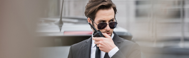 bodyguard in sunglasses and suit using walkie talkie outside, banner - Photo, Image