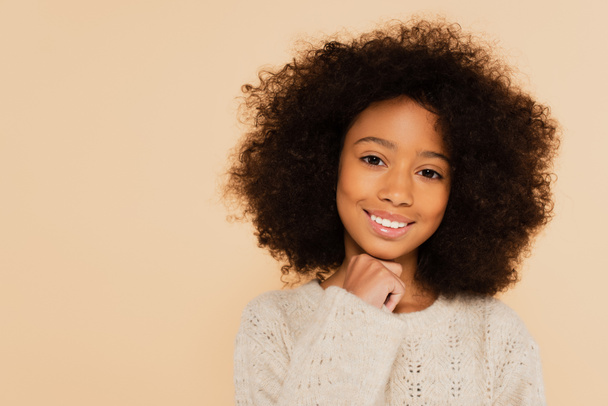 portrait of smiling preteen african american girl with hand near face isolated on beige - Foto, imagen