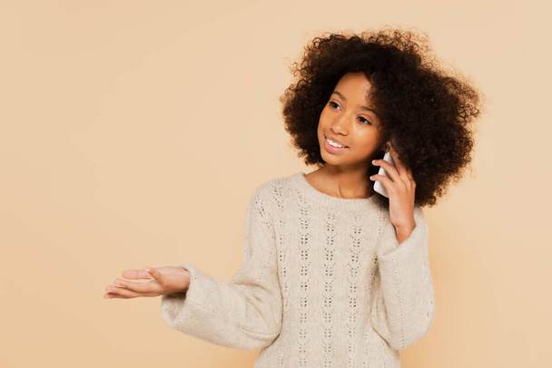 afro-americana preteen menina falando no celular e gesticulando isolado no bege - Foto, Imagem