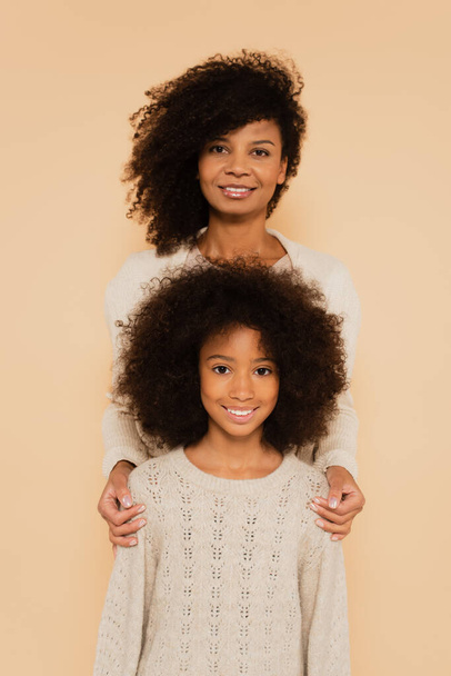 portrait of happy african american preteen daughter with mother isolated on beige - Fotó, kép