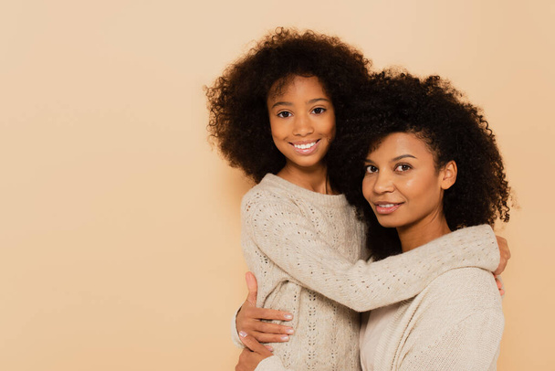afro-americana preteen filha e adulto mãe abraçando e sorrindo isolado no bege - Foto, Imagem