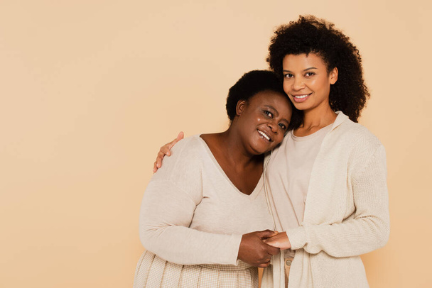 peaceful african american adult daughter and middle aged mother hugging isolated on beige - 写真・画像