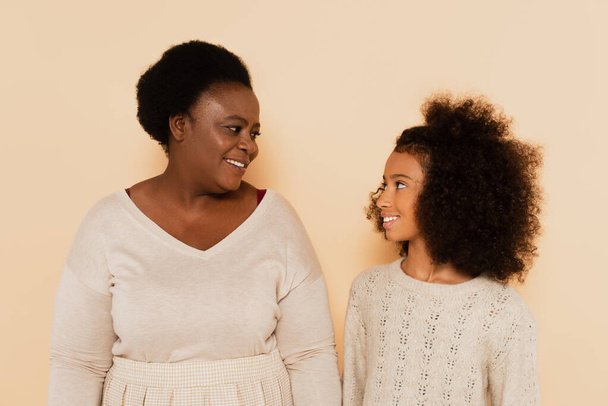 african american grandmother and granddaughter looking at each other on beige background - Photo, Image