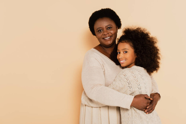 lächelnd afrikanisch-amerikanische Großmutter umarmt Enkelin auf beigem Hintergrund - Foto, Bild