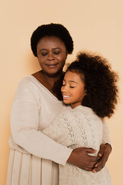 afroamericano nonna abbracciare nipote con gli occhi chiusi su sfondo beige - Foto, immagini