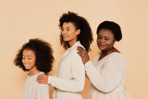 afrikanisch-amerikanische Tochter, Mutter und Großmutter halten einander die Hände auf den Schultern isoliert auf beige - Foto, Bild