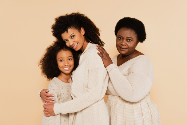 african american grandmother embracing with smiling daughter and granddaughter isolated on beige - Foto, immagini