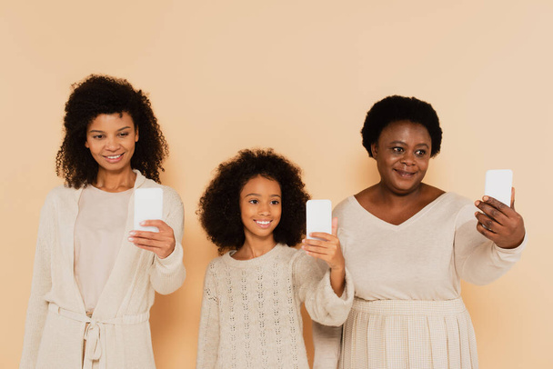 african american daughter, granddaughter and grandmother taking selfies on cellphones on beige background - Photo, Image