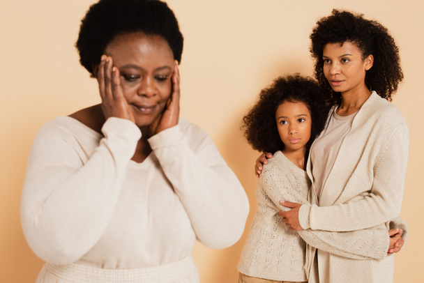 african american mother embracing with daughter and looking at disappointed grandmother with hands near head on beige background - Fotografie, Obrázek
